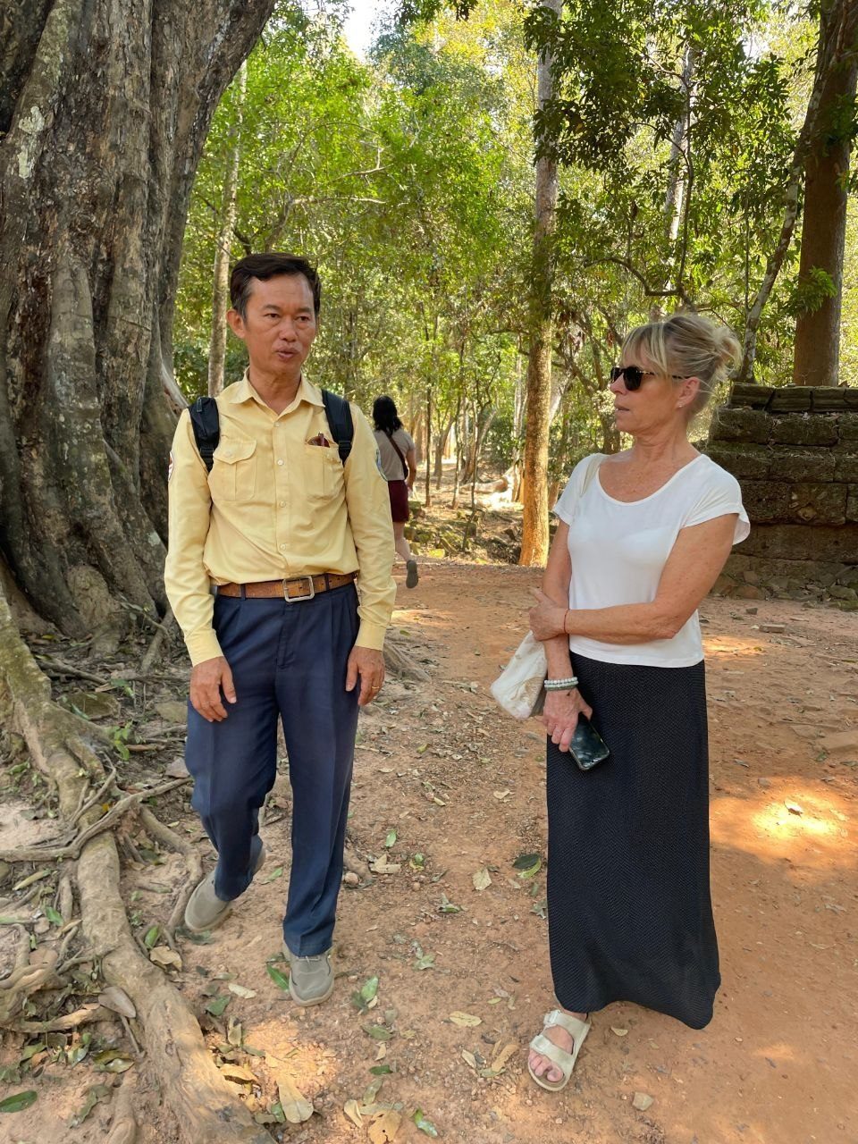 Le guide accompagnant une voyageuse sur un sentier ombragé du Cambodge